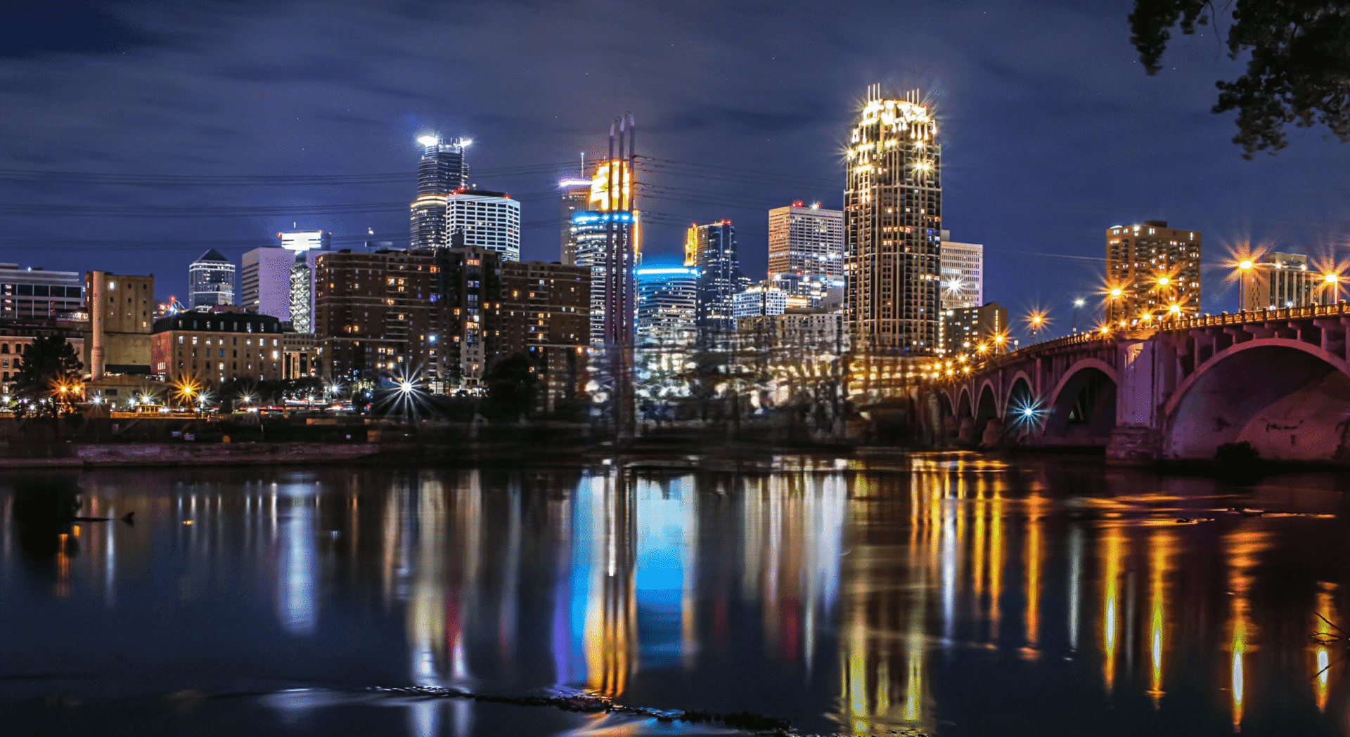 City skyline at night with illuminated buildings reflecting on water.