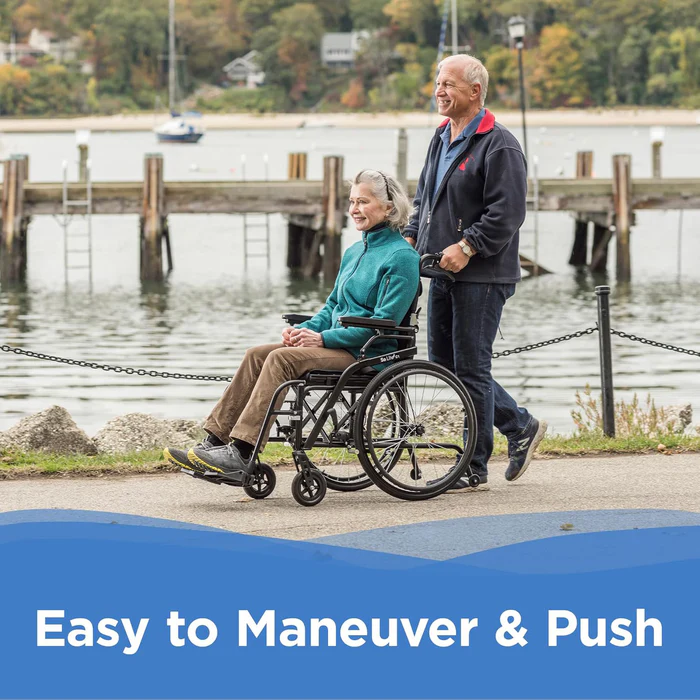 Person pushing another in wheelchair by a waterfront.