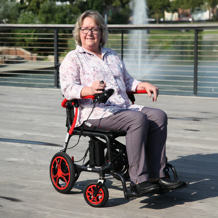 A woman smiling while sitting in a modern wheelchair outdoors by the water.