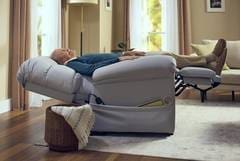 A man laying on top of a recliner in a living room.