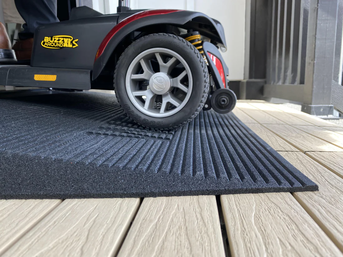 A wheelchair wheel on a textured mat over wooden flooring.