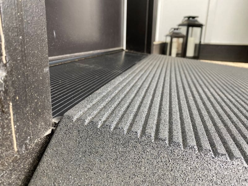 Close-up of a textured black floor mat near a doorway.