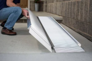 Person unfolding a portable wheelchair ramp outside a building.