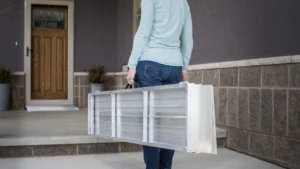 Person carrying a folded white ladder outdoors.