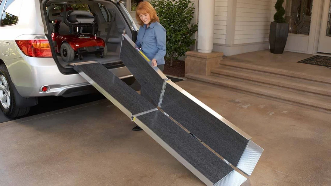 Person setting up a foldable ramp from a car trunk.