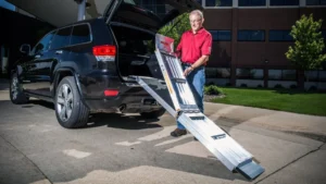 Man using a ramp to load a wheelchair into a car.