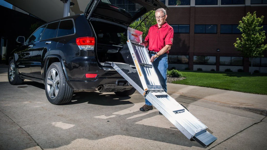 Man using a ramp to load a wheelchair into a car.