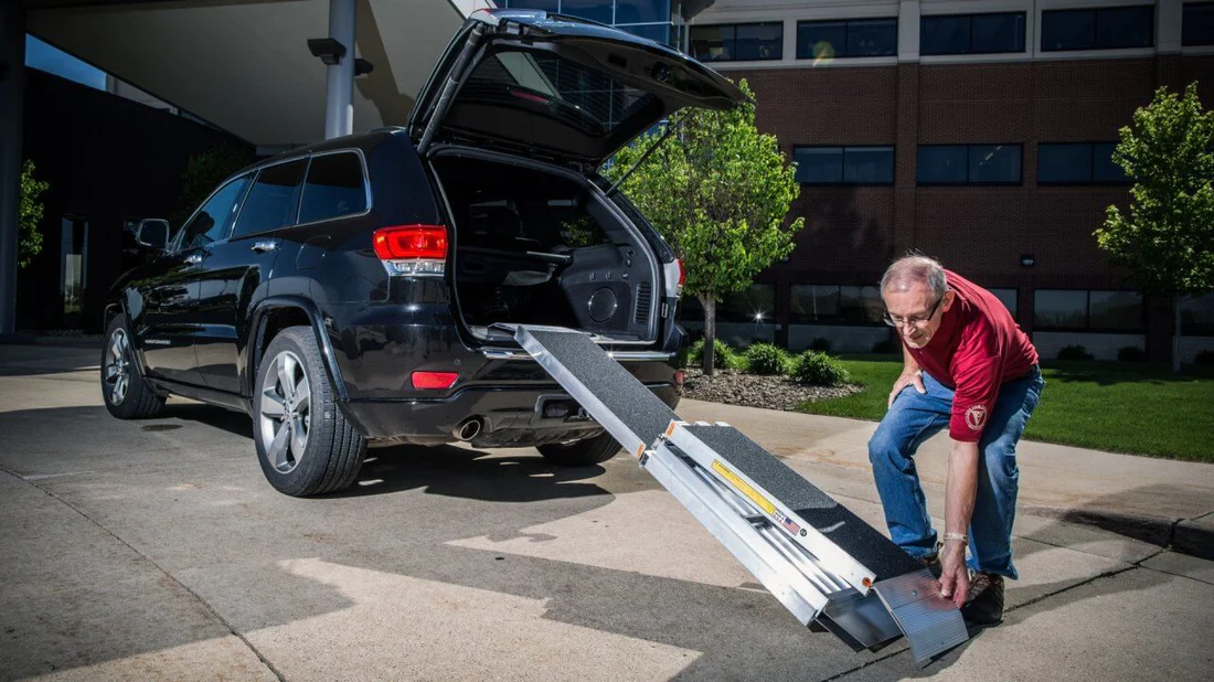 Man loading items into a black SUV using a ramp.