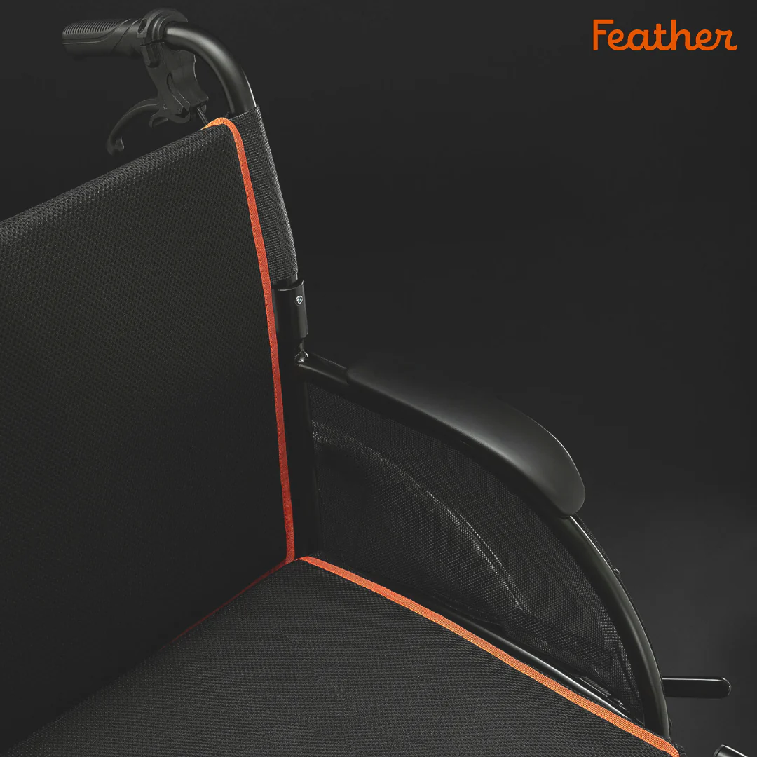 Black wheelchair with orange trim against a dark background.