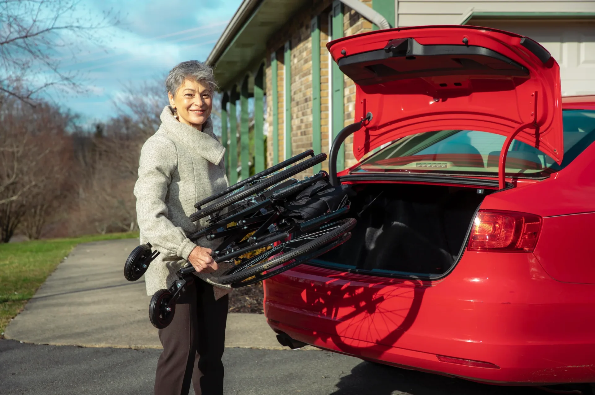 Woman unloading a folding chair from a red car's trunk.
