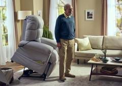 Man operating a motorized lift recliner chair in a living room.