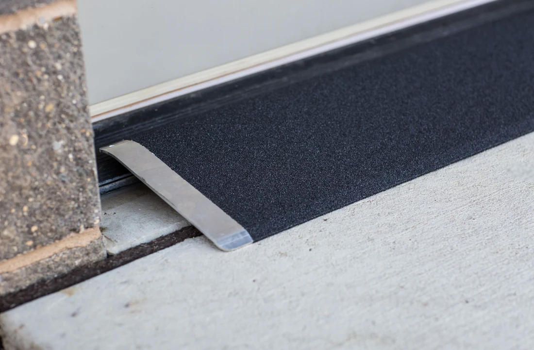 Metal threshold strip securing a black floor mat edge.