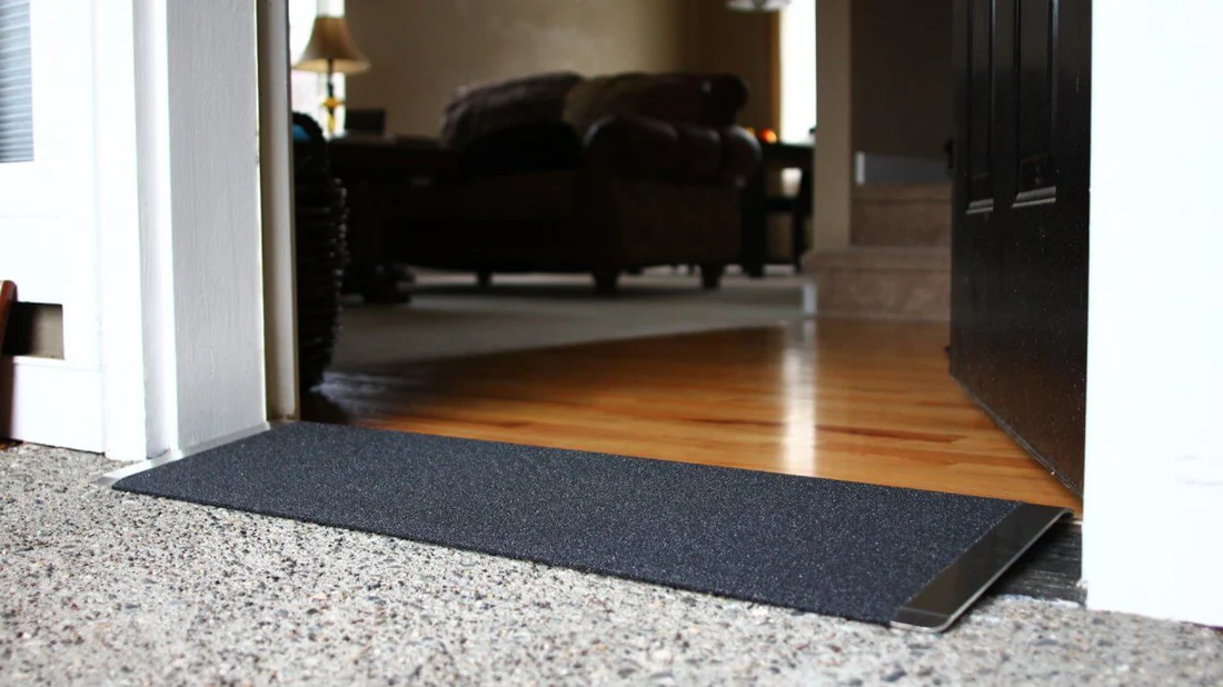 A close-up of a carpet edge with a wooden floor and furniture in the background.