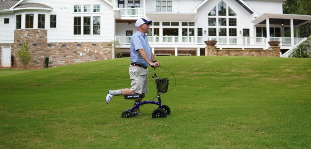 Man using a knee scooter on grass near a house.