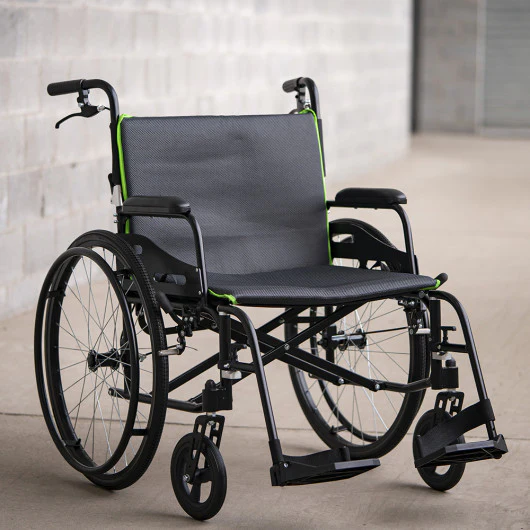 A black wheelchair with green accents on a smooth floor indoors.