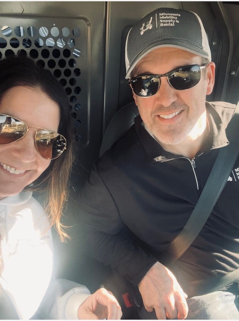 A smiling couple wearing sunglasses inside a vehicle.