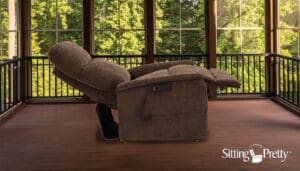 A plush recliner chair in a cozy room with large windows showing green trees outside.