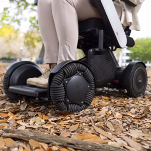 Close-up of a person using an all-terrain wheelchair on a leaf-covered path.