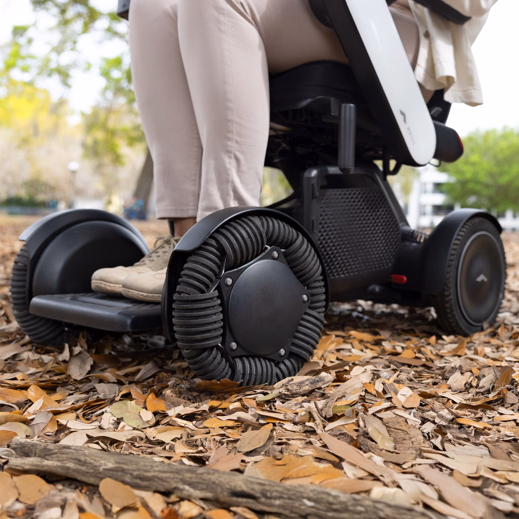 Close-up of a person using an all-terrain wheelchair on a leaf-covered path.