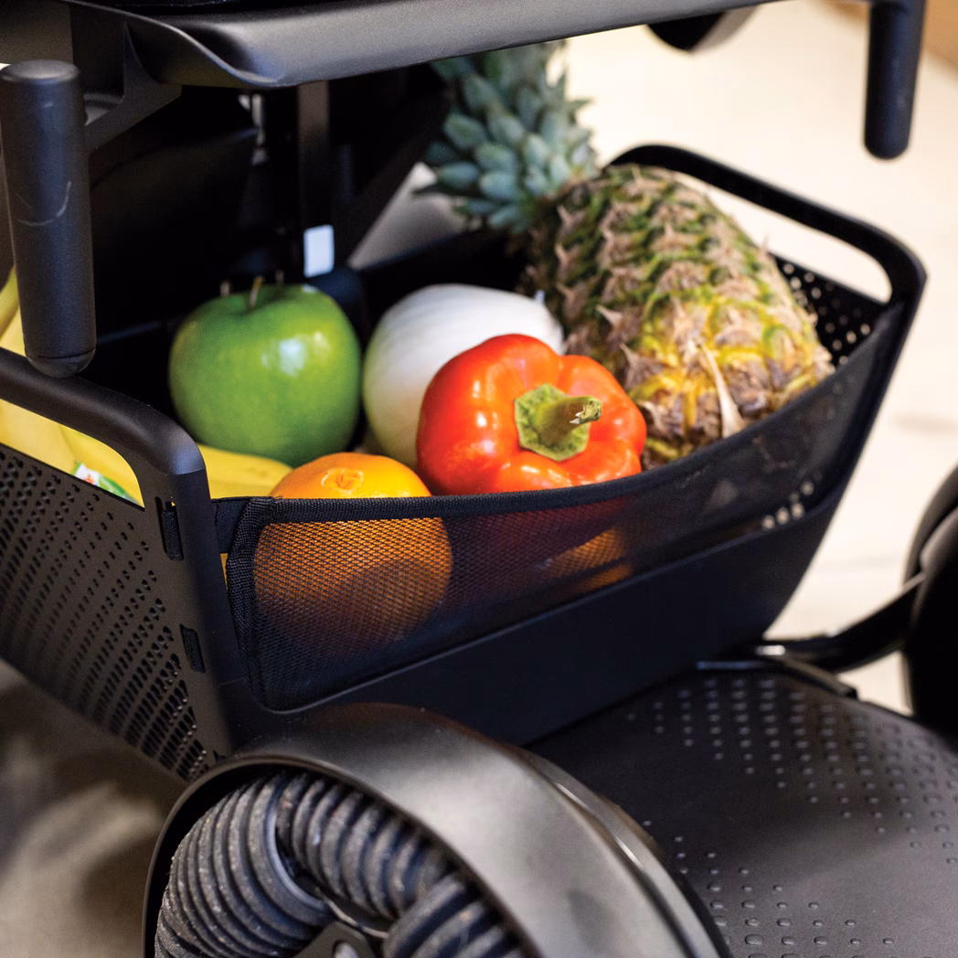 A basket with fruits on a wheelchair, including pineapple and apple.