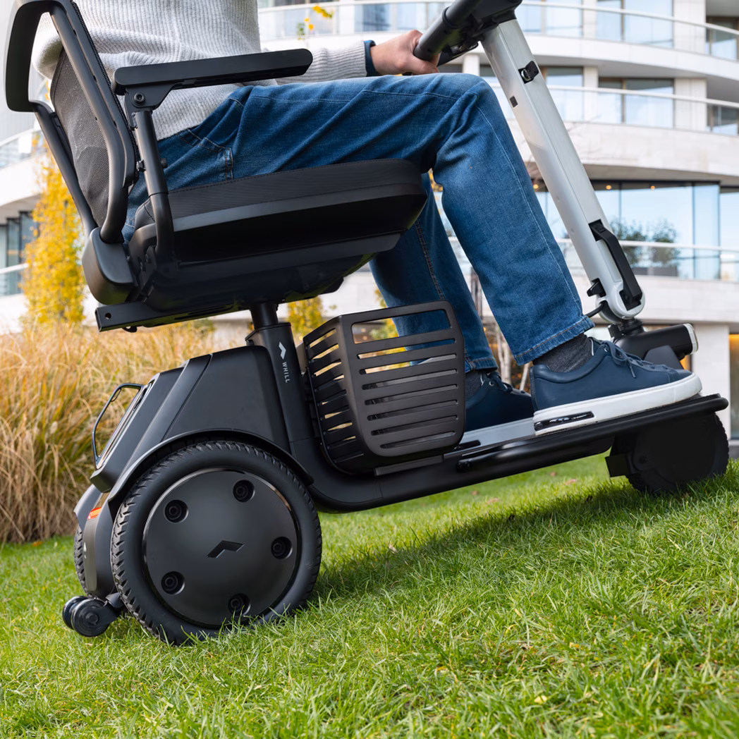 Person sitting on a mobility scooter on grass.